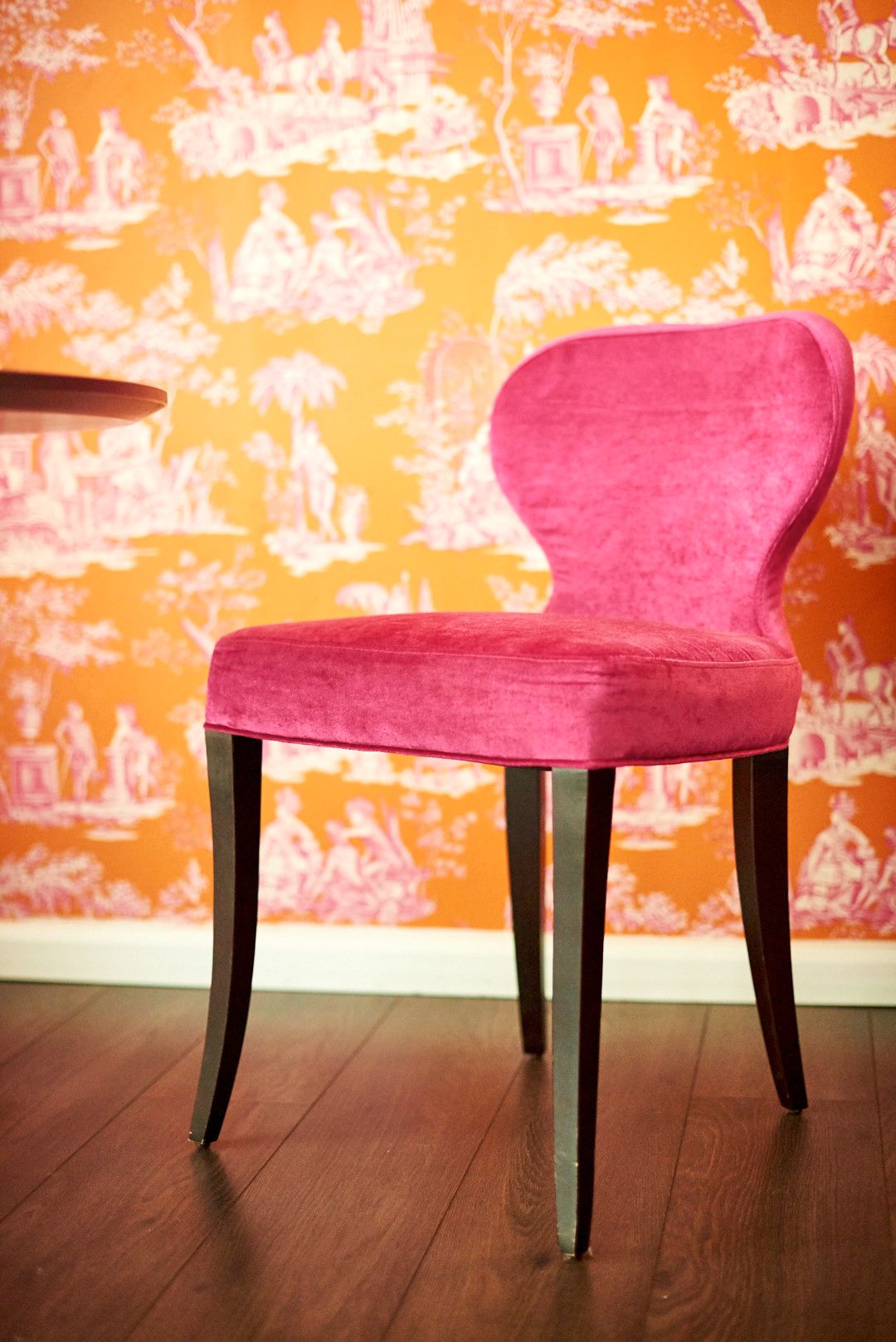 Pink velvet accent chair against vibrant orange patterned wall.