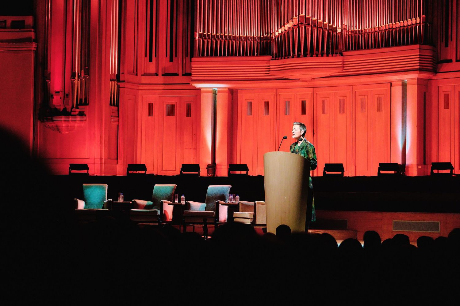 Concert hall interior with red-lit pipe organ and seating.