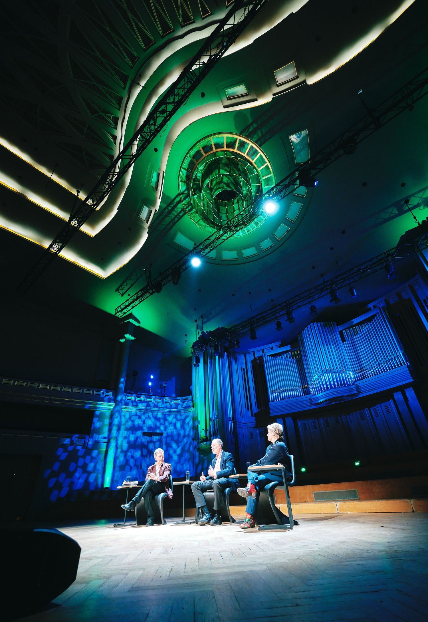 Modern auditorium with dramatic green and blue lighting during a panel discussion.
