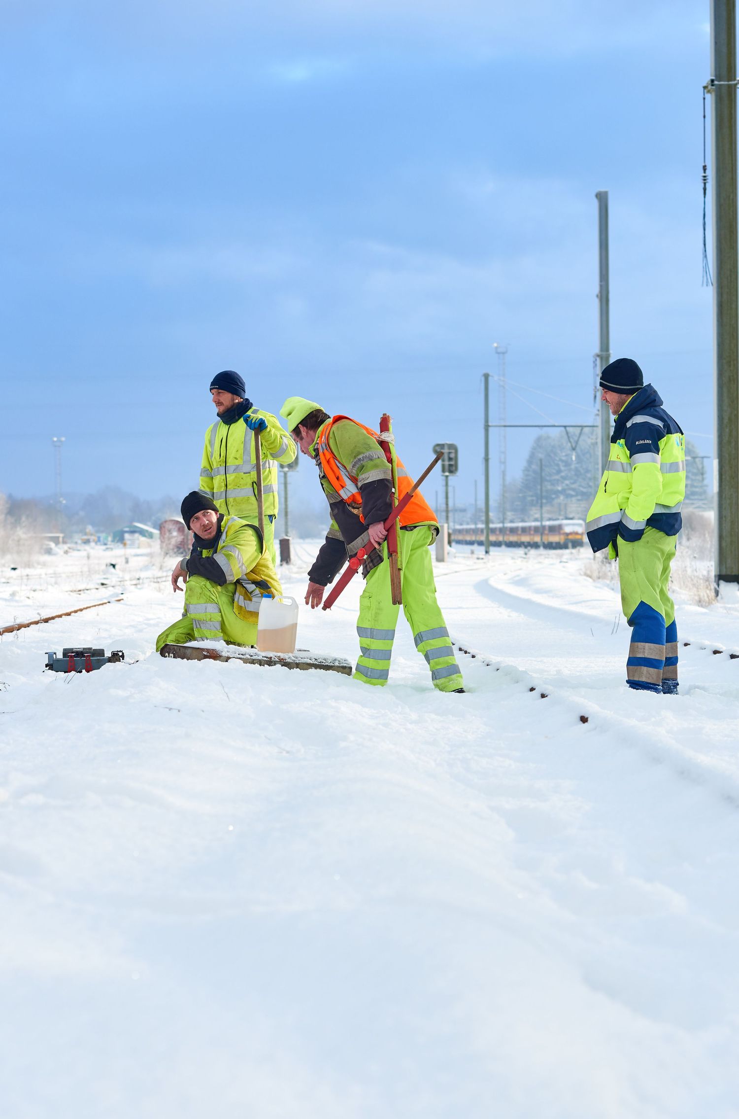 Railway workers in high-visibility gear maintain snow-covered train tracks during winter conditions.