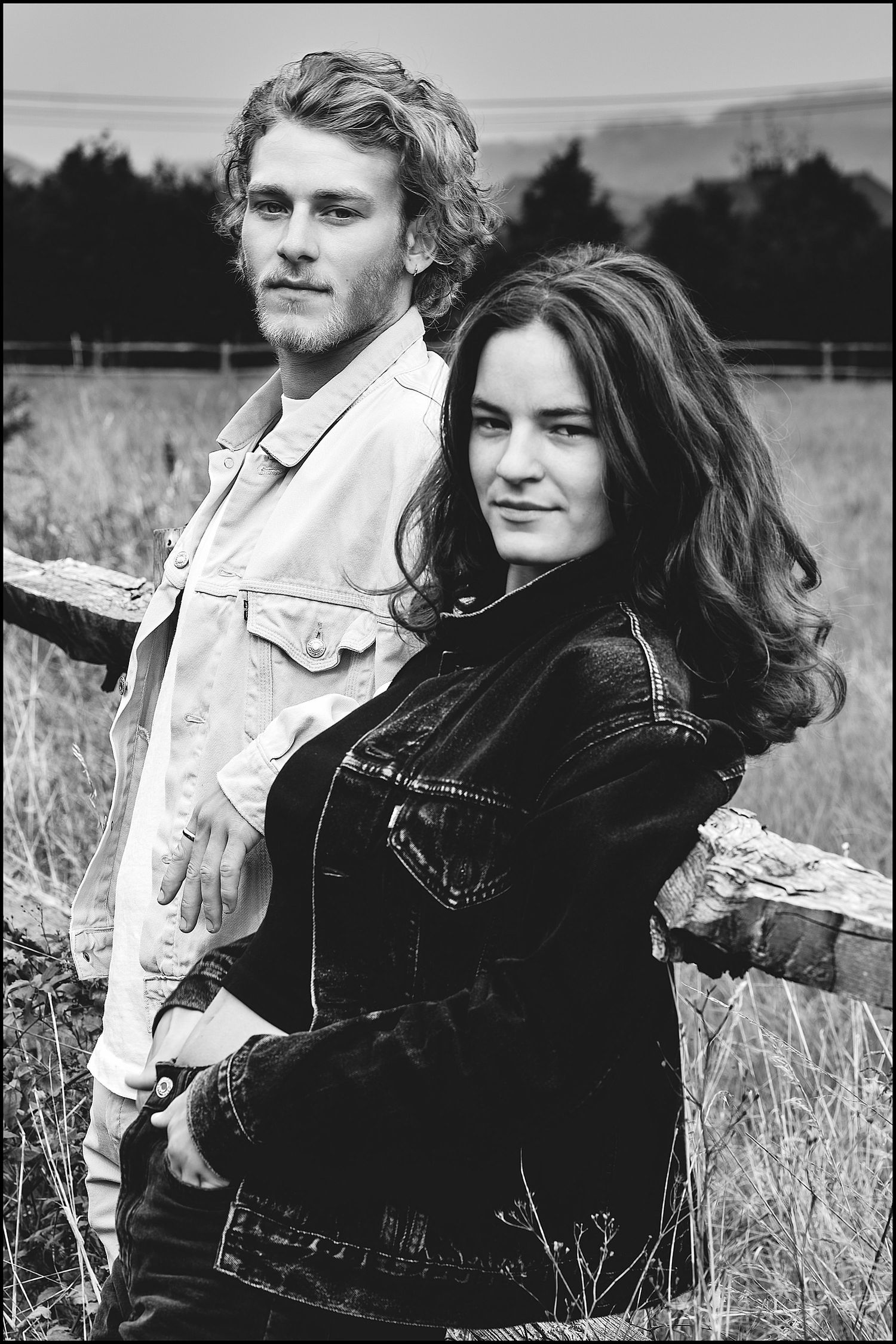 Candid black and white photo of a couple sitting in a grassy field wearing denim jackets.