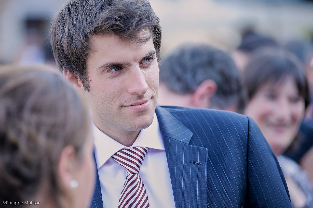 Elegant man in pinstripe suit and striped tie smiling at an outdoor wedding reception.