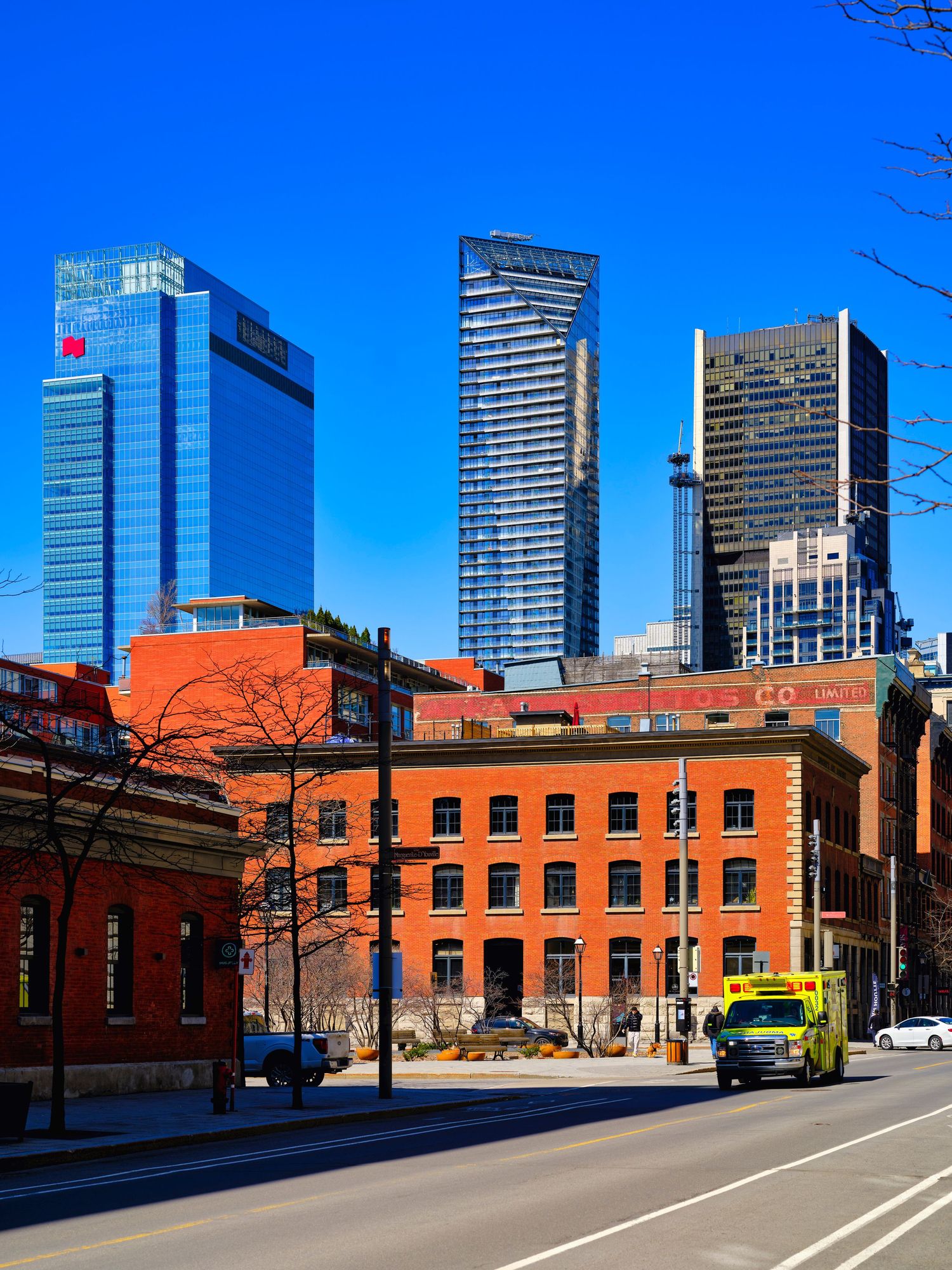 Historic red brick buildings contrast with modern glass skyscrapers in an urban cityscape against bright blue sky.