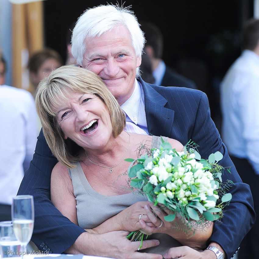 Happy older couple embracing at a wedding, woman holding white floral bouquet, both smiling joyfully.
