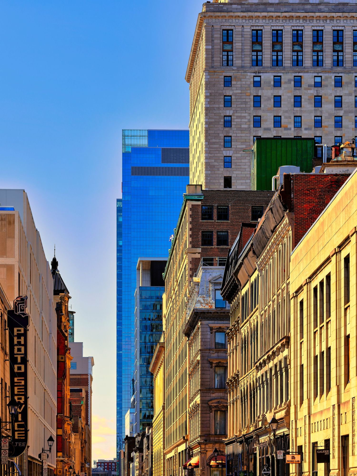 Historic brick buildings and modern skyscrapers line a city street under bright blue skies.