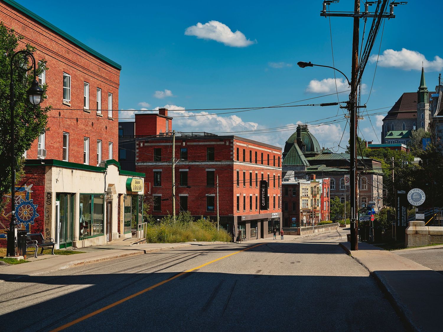 Historic red brick buildings and storefronts line a quiet small town main street.