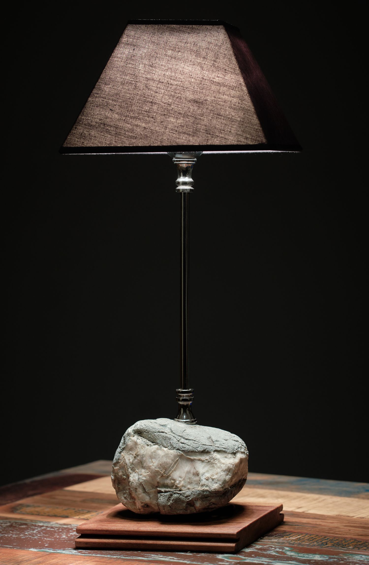 A modern table lamp with a stone base and beige shade on a wooden surface.