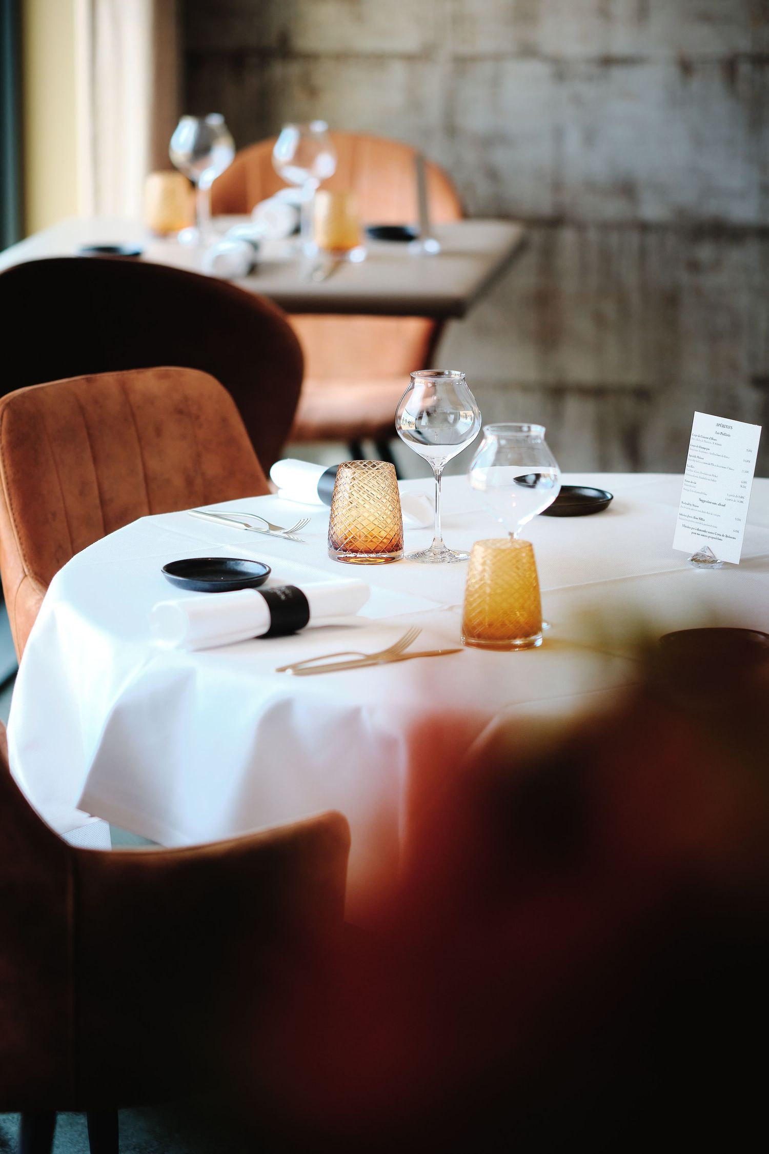 Elegant restaurant table setting with white tablecloth and brown leather chairs in soft focus.