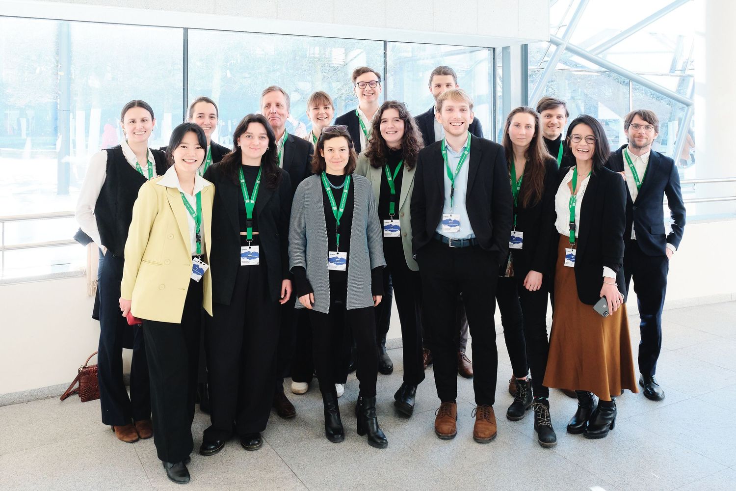 Group photo of business professionals in formal attire in bright modern hallway.