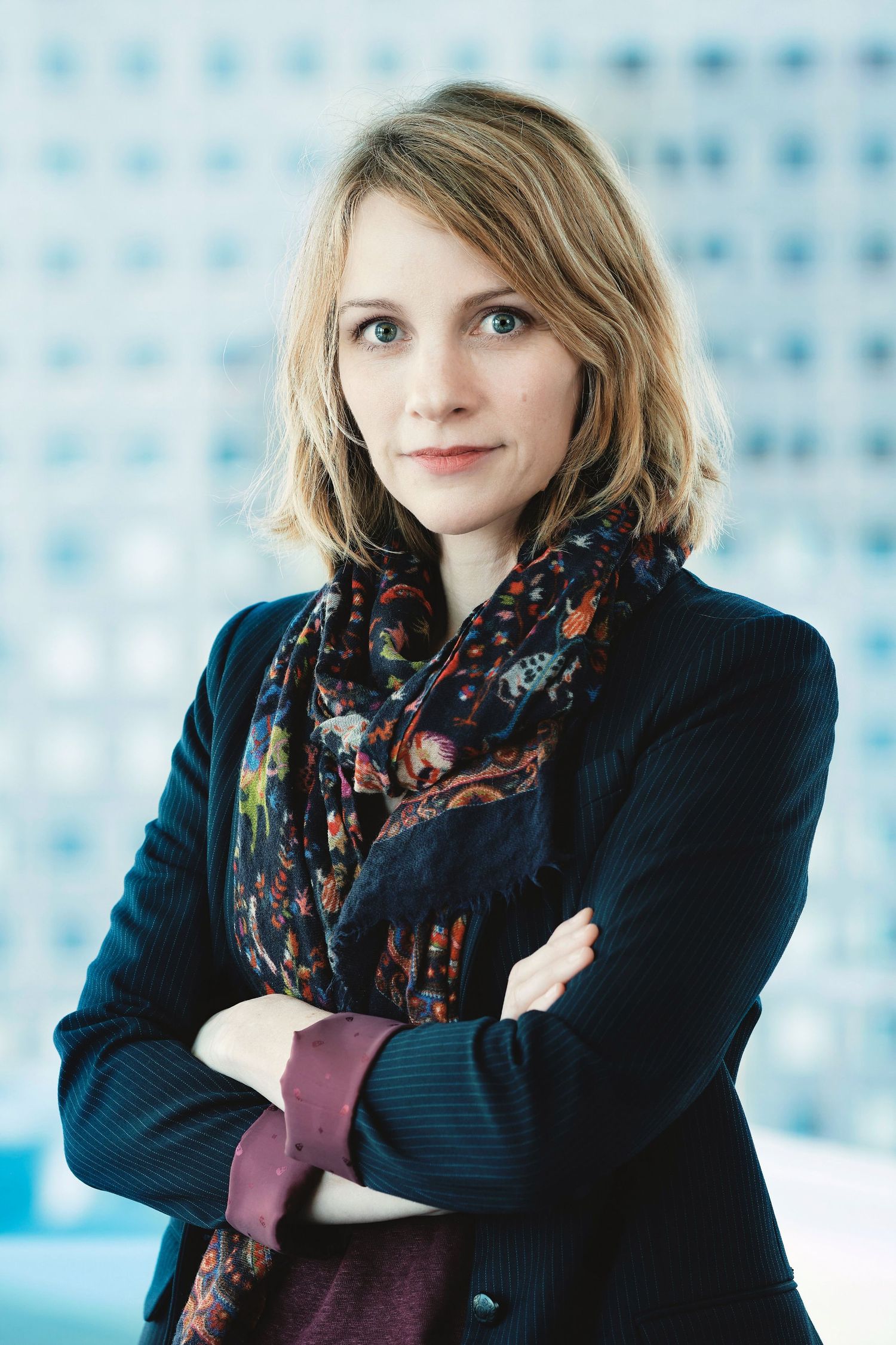 Professional portraits in navy blazer and patterned scarf against blue geometric background.