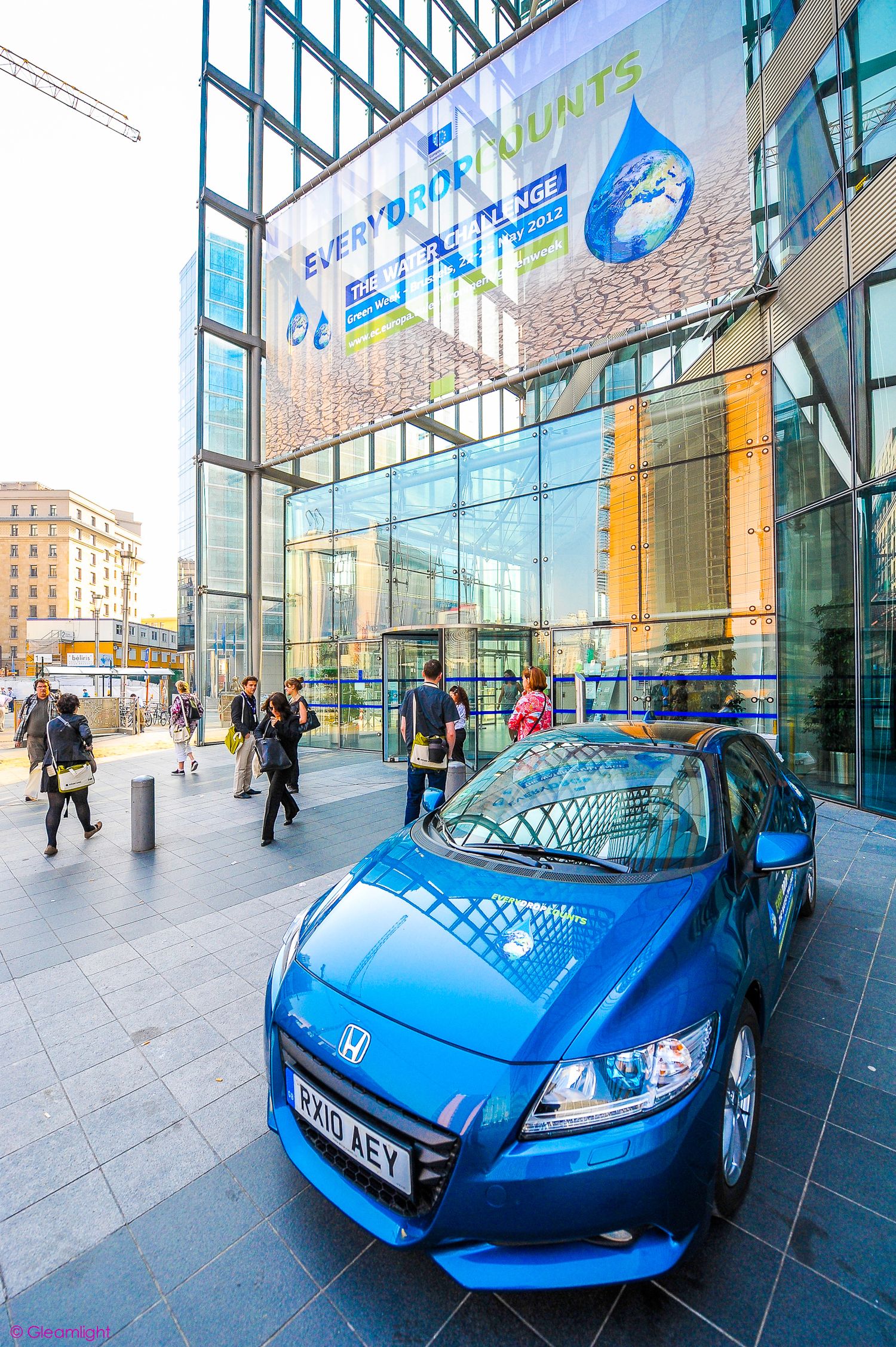 Blue sports car displayed in front of a modern glass building entrance.