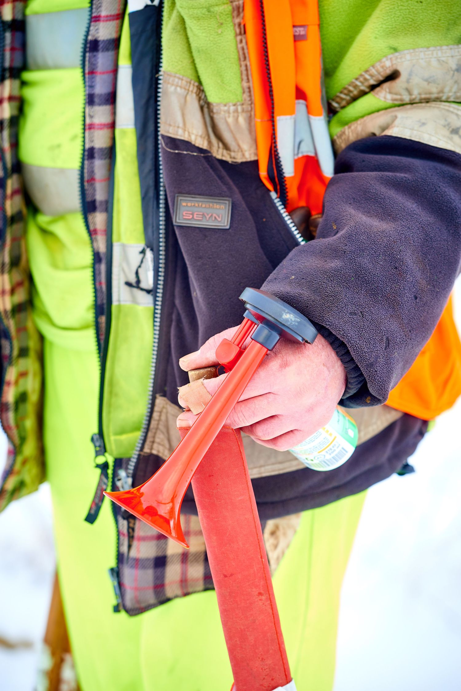 Close-up of worker wearing high visibility vest holding safety equipment.