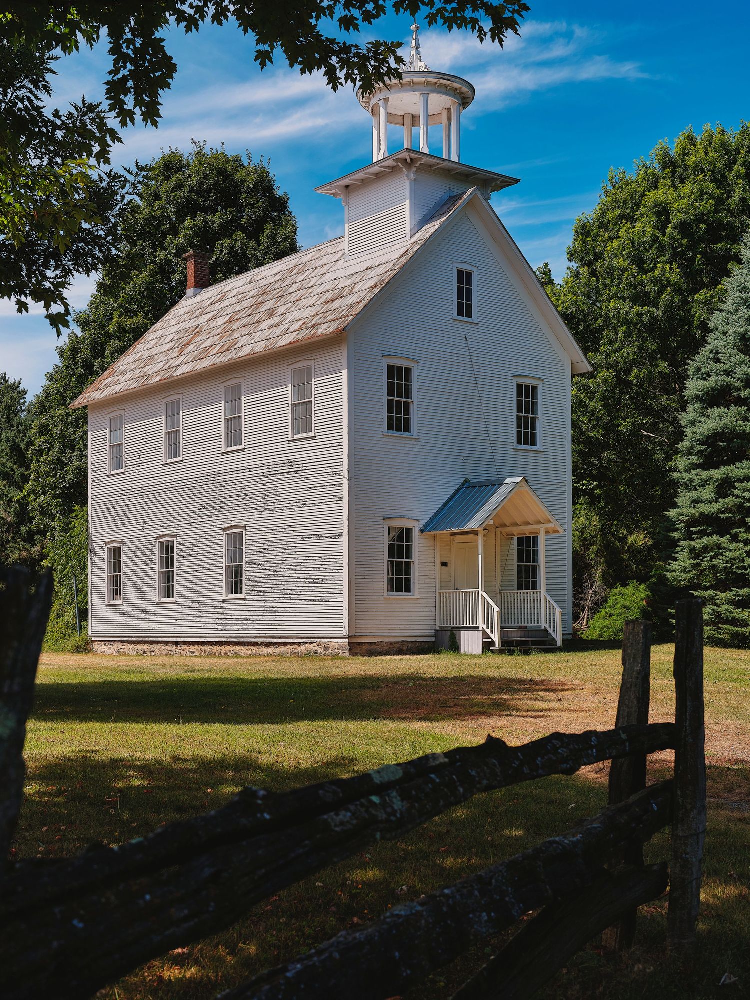 Historic white wooden church building with cupola stands in a grassy field on a sunny day.