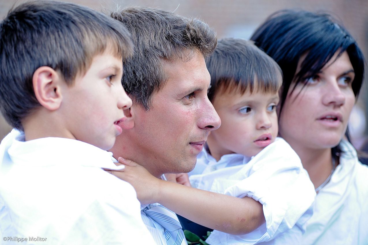 Family portrait of father, mother, and two young boys in white shirts at outdoor event.