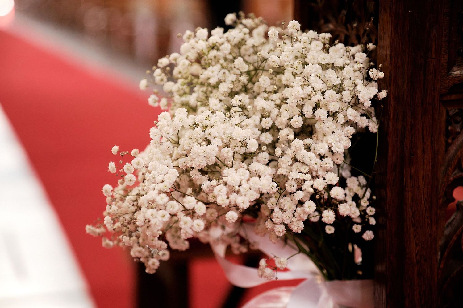 Delicate white baby's breath flowers arranged in a bouquet, decorating a wooden church pew at a wedding ceremony.