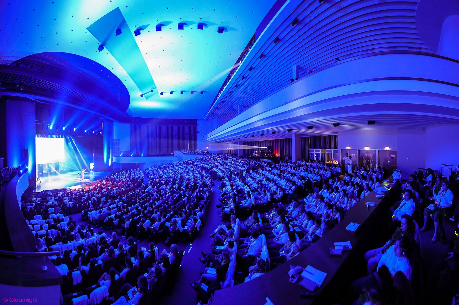 Large conference hall with blue lighting and packed audience during international event.