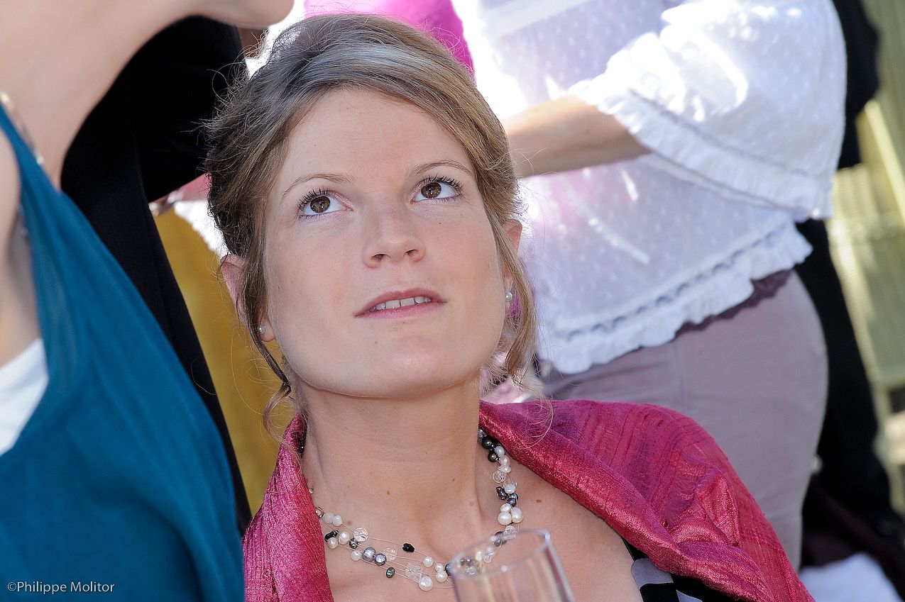 Elegant young woman in pink jacket with pearl necklace gazing upward at an outdoor event.