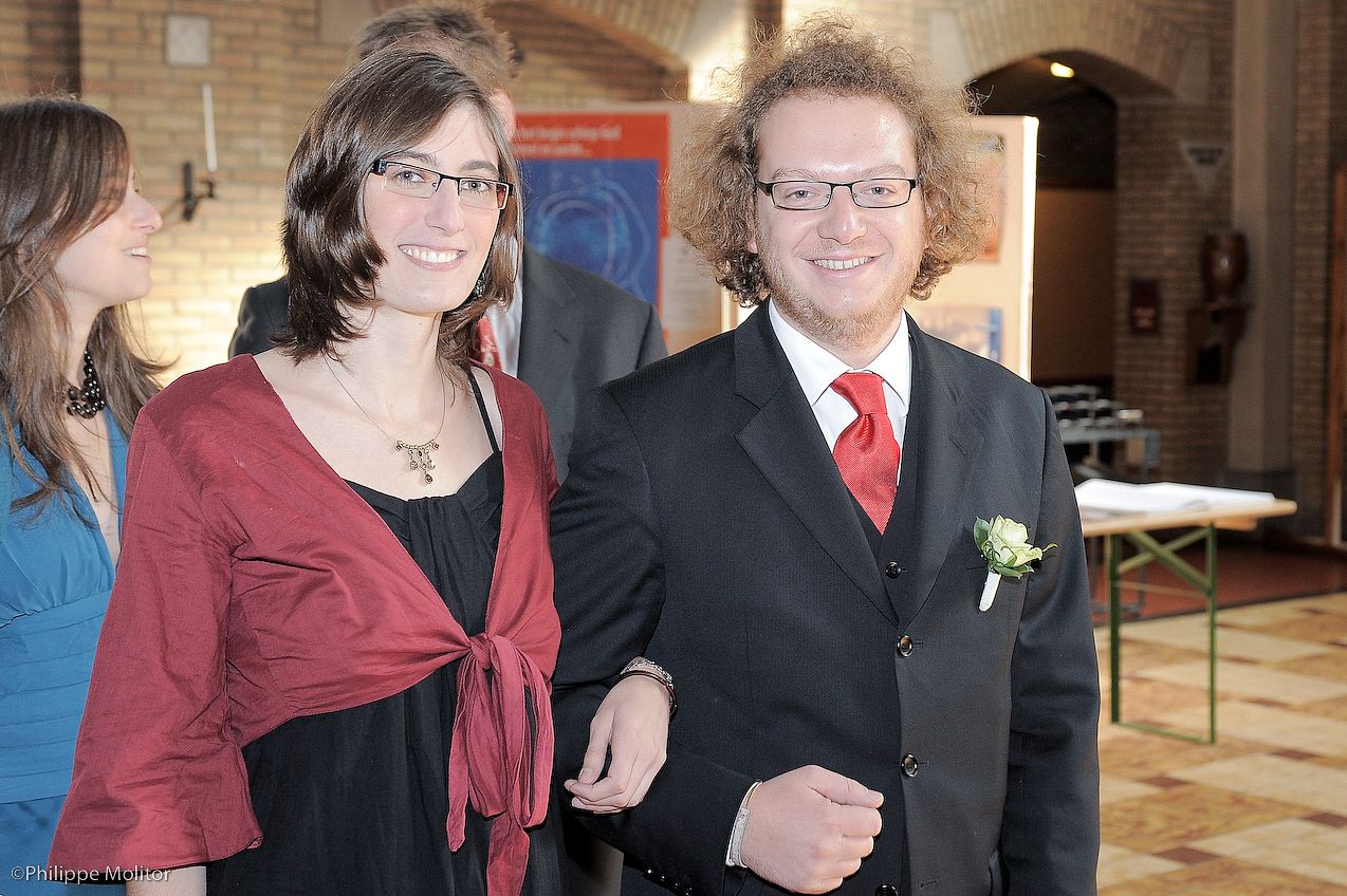 Smiling couple posing together at a wedding reception, man in black suit with red tie and boutonniere.