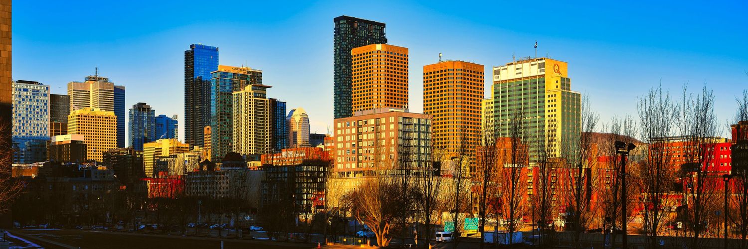 Panoramic view of Calgary's downtown skyline with modern skyscrapers against blue sky during autumn.