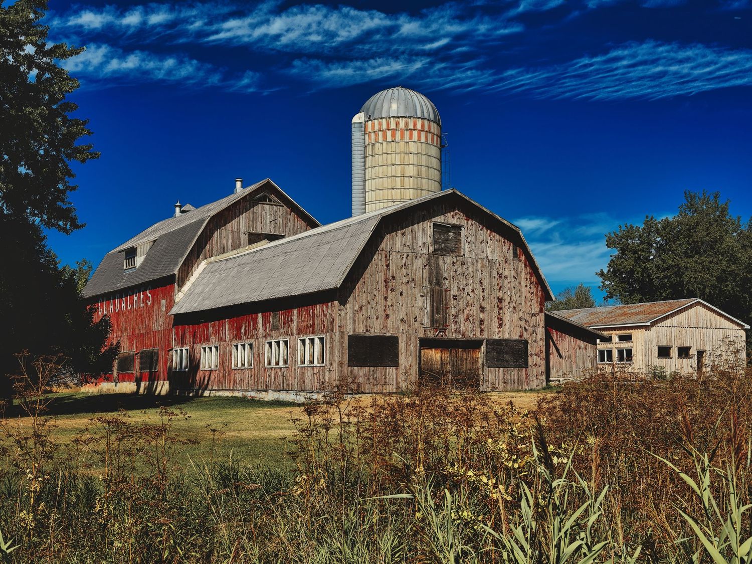Panoramic view of red barns and silos along a rural hillside during autumn season.