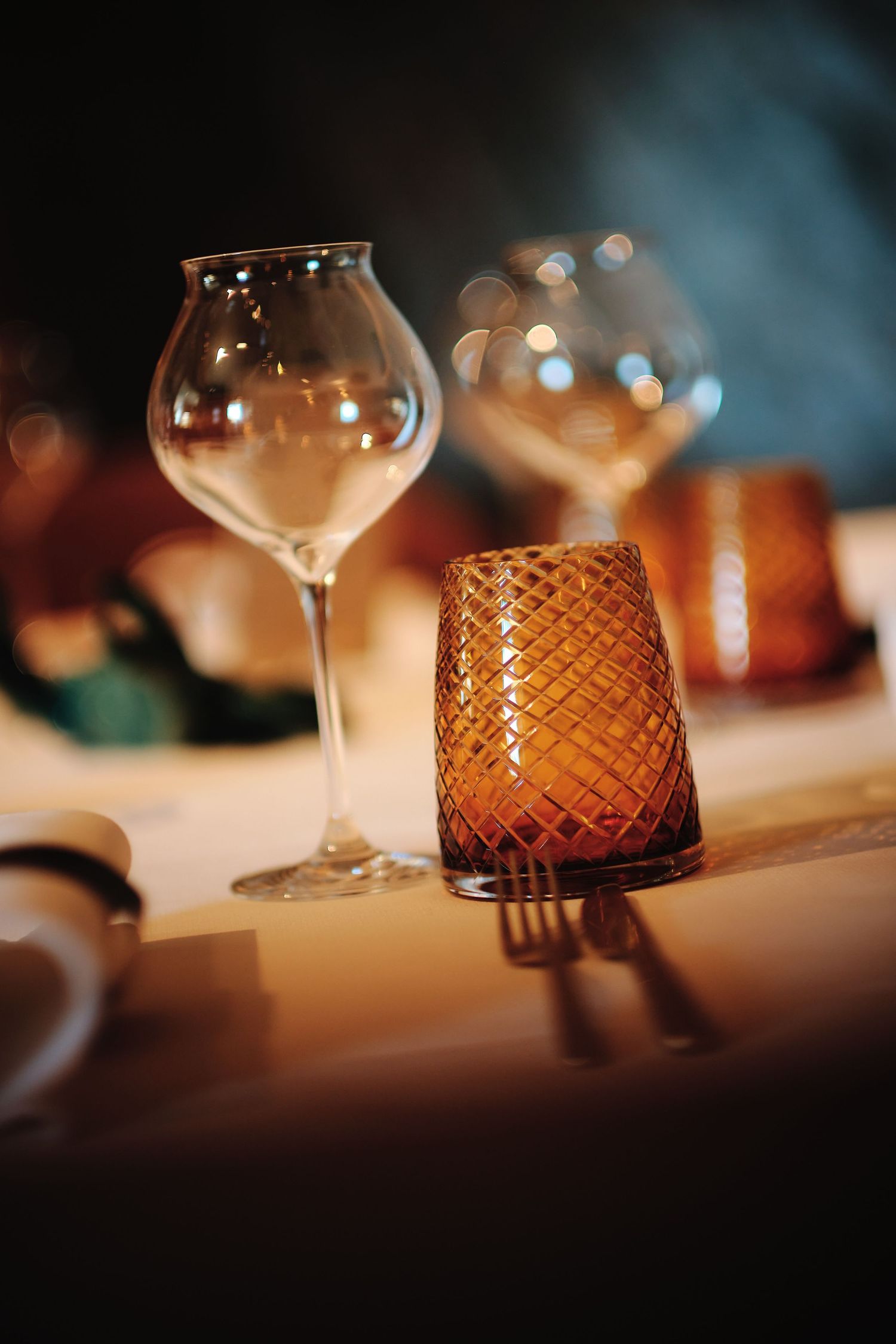 Elegant wine glasses and amber-colored glass vases arranged on a dining table with soft lighting and bokeh effects.