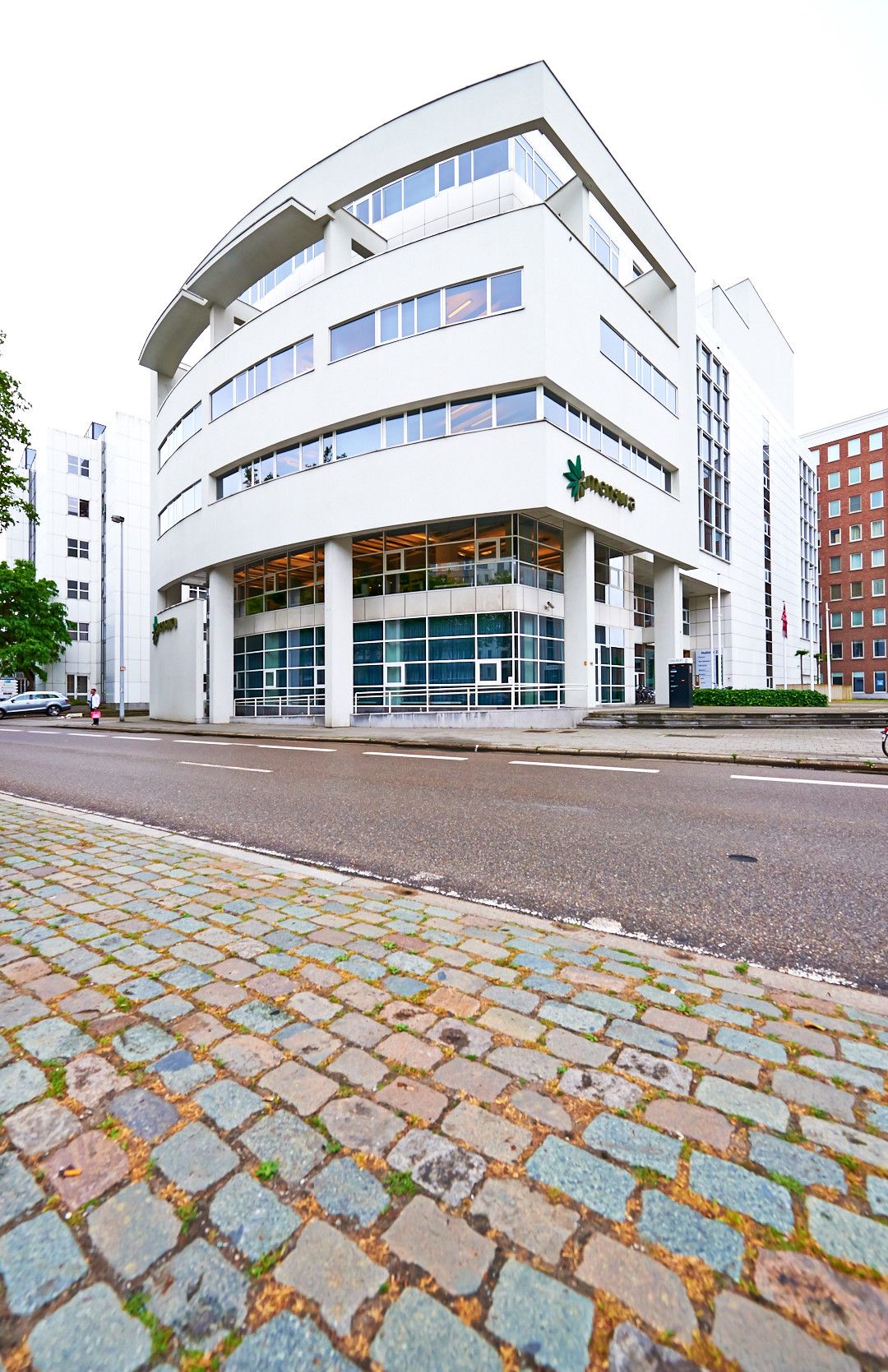 Striking white modern building with curved facade and glass windows on cobblestone street.
