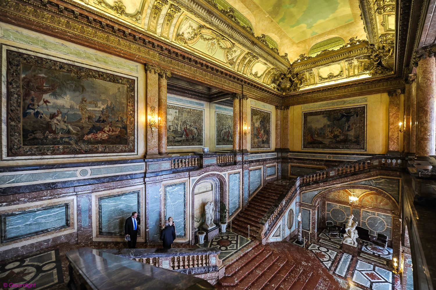 Ornate historic palace room with gilded ceiling and classical paintings in panoramic view.