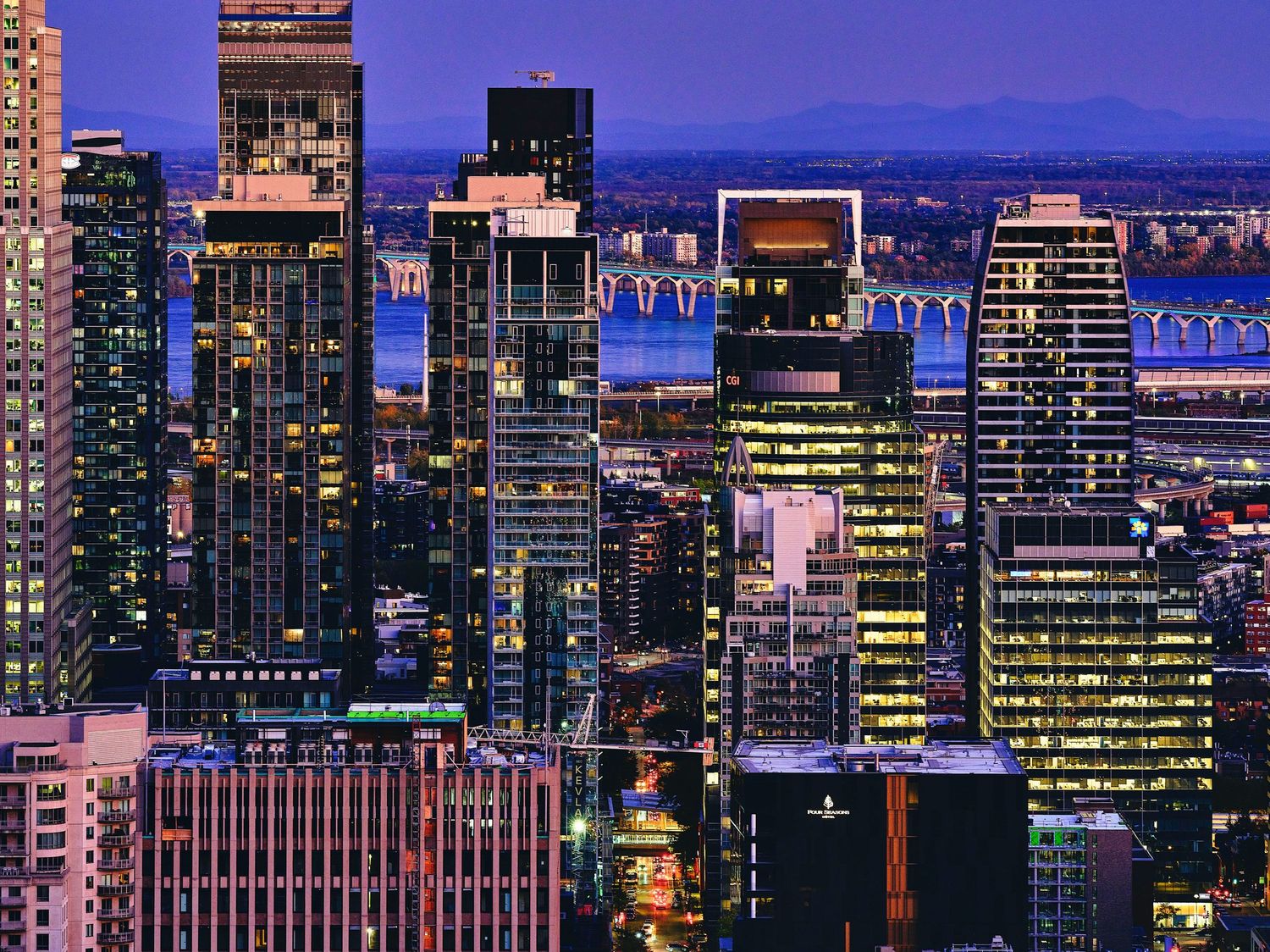 Purple sunset sky frames modern city skyline with illuminated high-rise buildings.