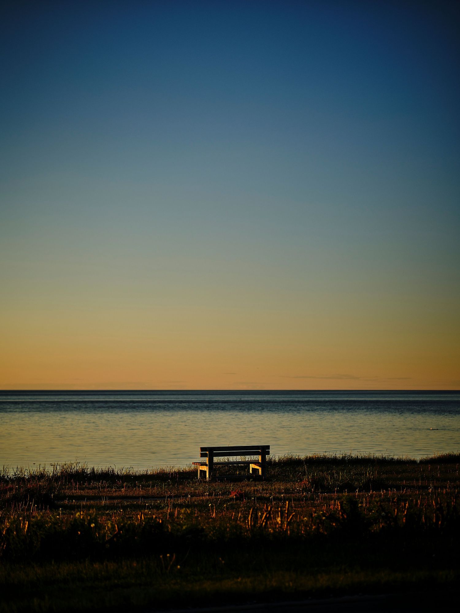 Silhouette of a bench against an ocean horizon during golden hour sunset.