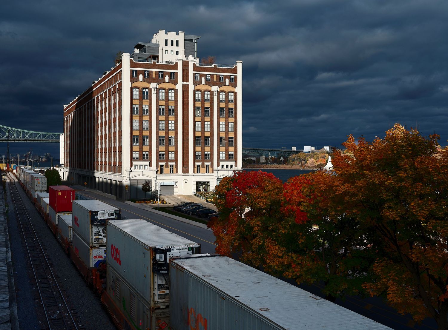 Panoramic cityscape of Montreal's waterfront with fall foliage and industrial buildings under moody skies.