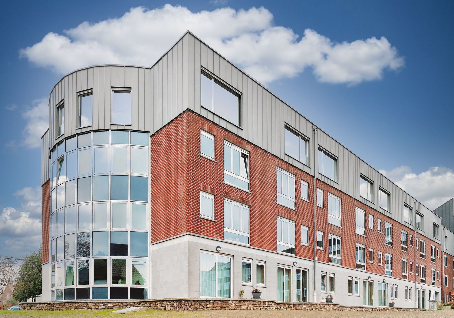 Modern commercial building exterior with red brick and curved glass windows under blue sky.