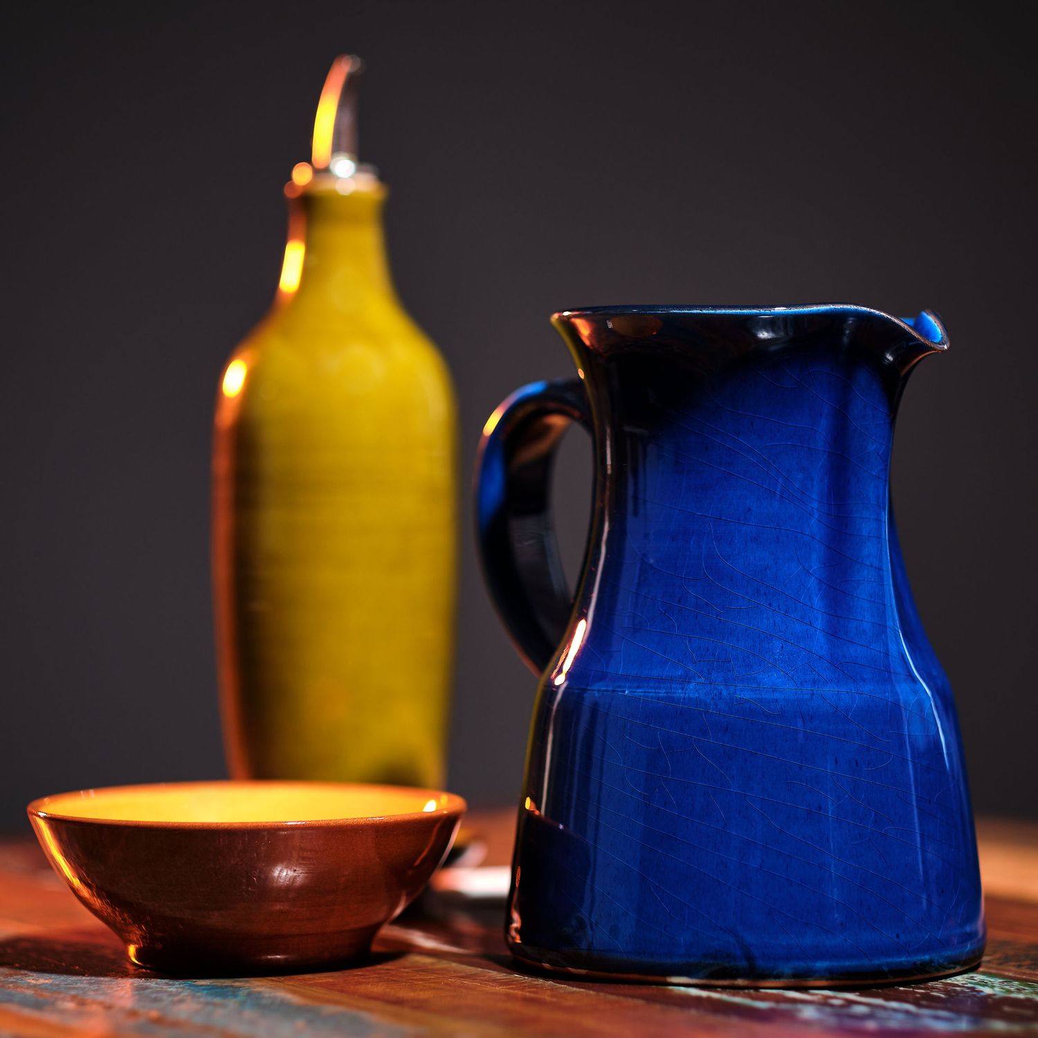 Yellow bottle and blue ceramic pitcher arranged artistically on a rustic wooden surface in dramatic lighting.
