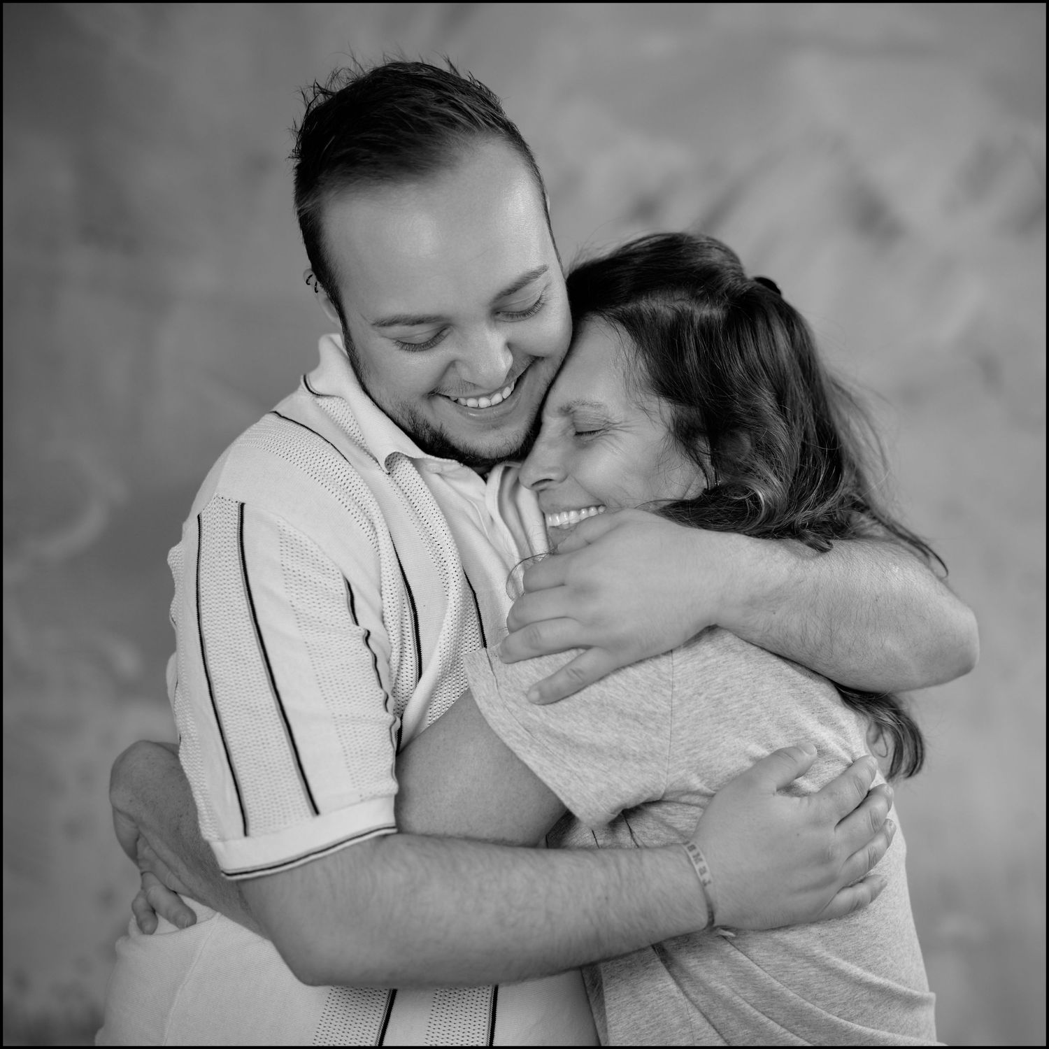 A smiling man and woman share a warm embrace in a black and white portrait photo.