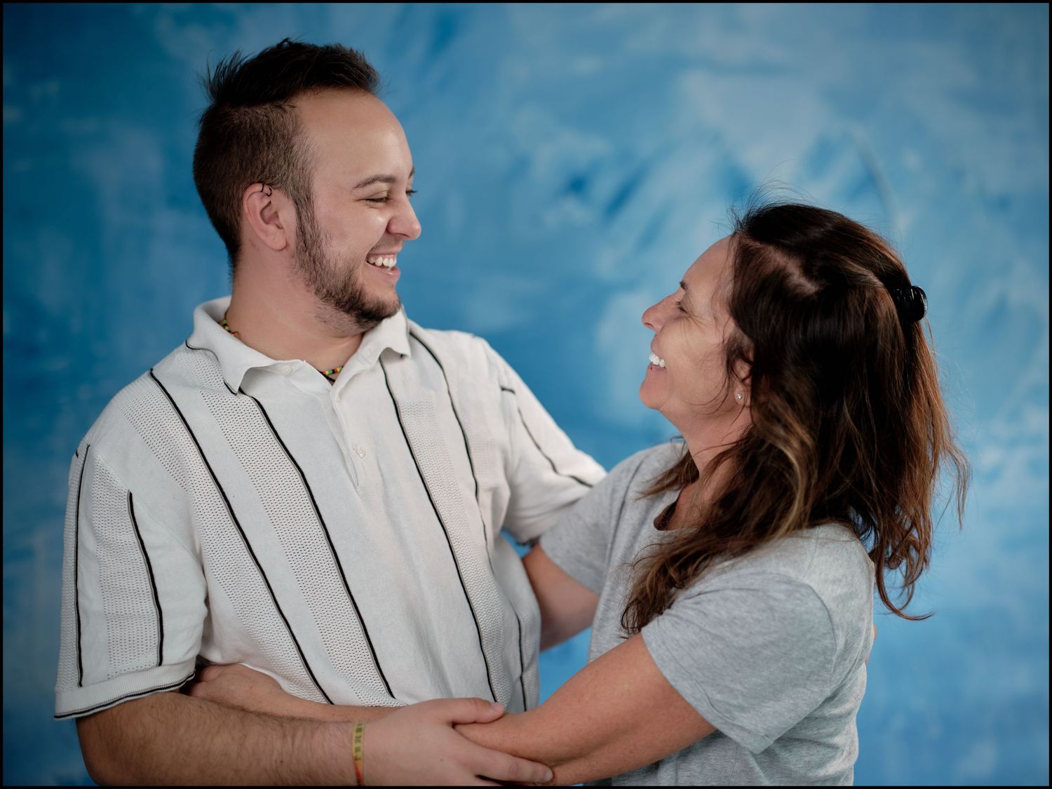 A smiling couple holds each other and gazes into each other's eyes against a blue background.