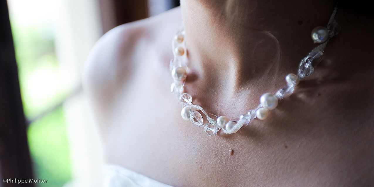 Close-up of an elegant bridal pearl and wire necklace worn by a bride in a white dress.