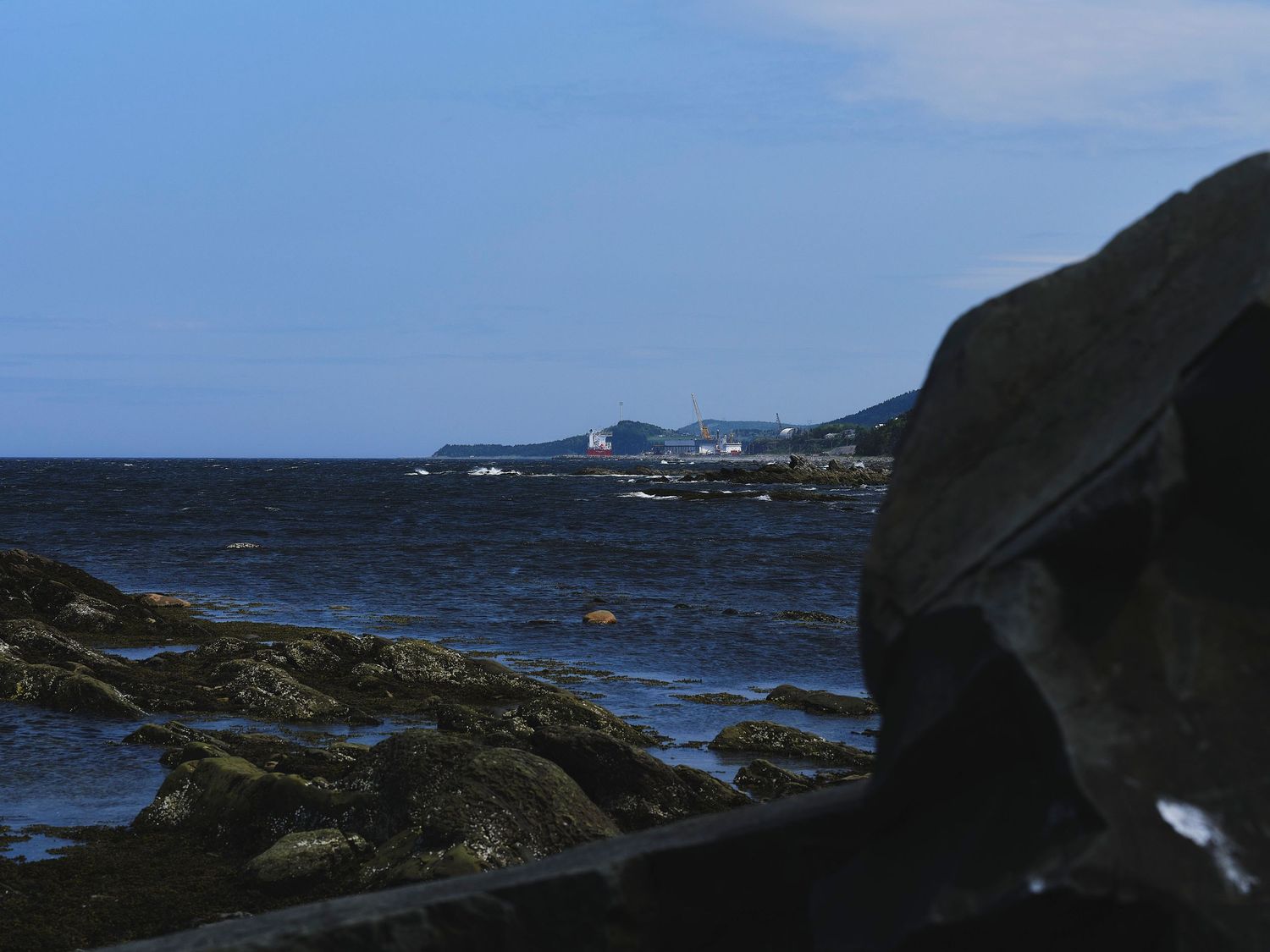 Rocky coastal shoreline with dark waters and distant hills under a moody blue sky.