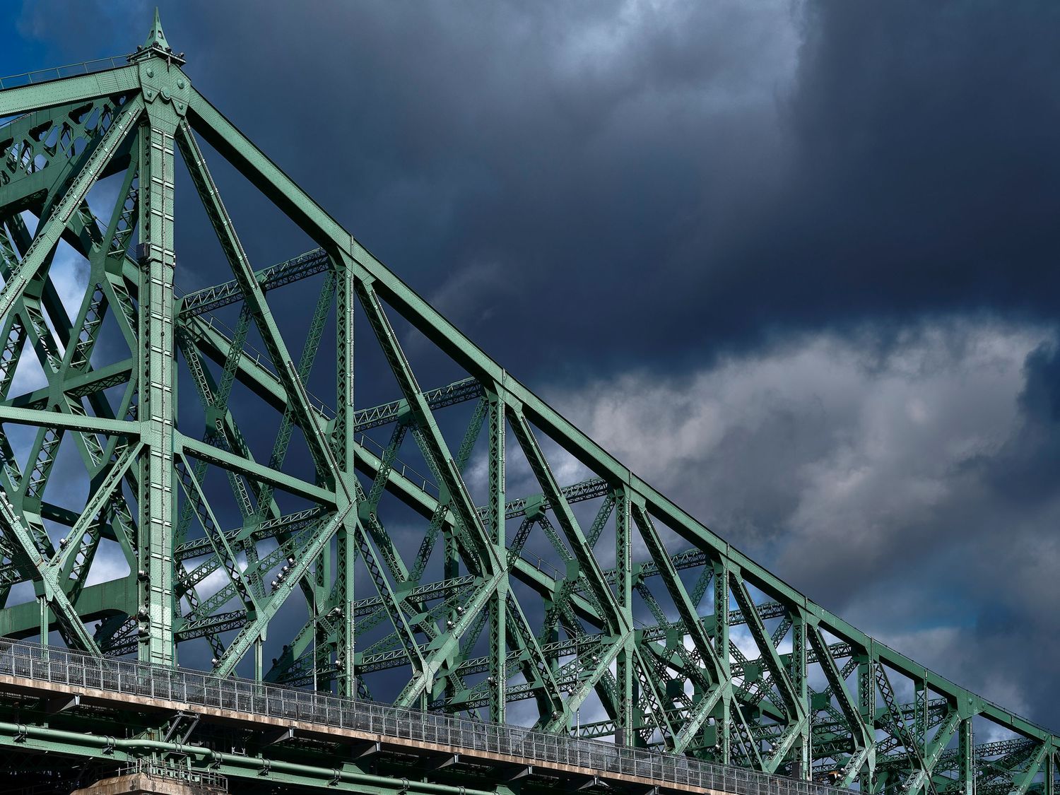 Dark storm clouds gather dramatically over a series of green steel bridge trusses and support beams.