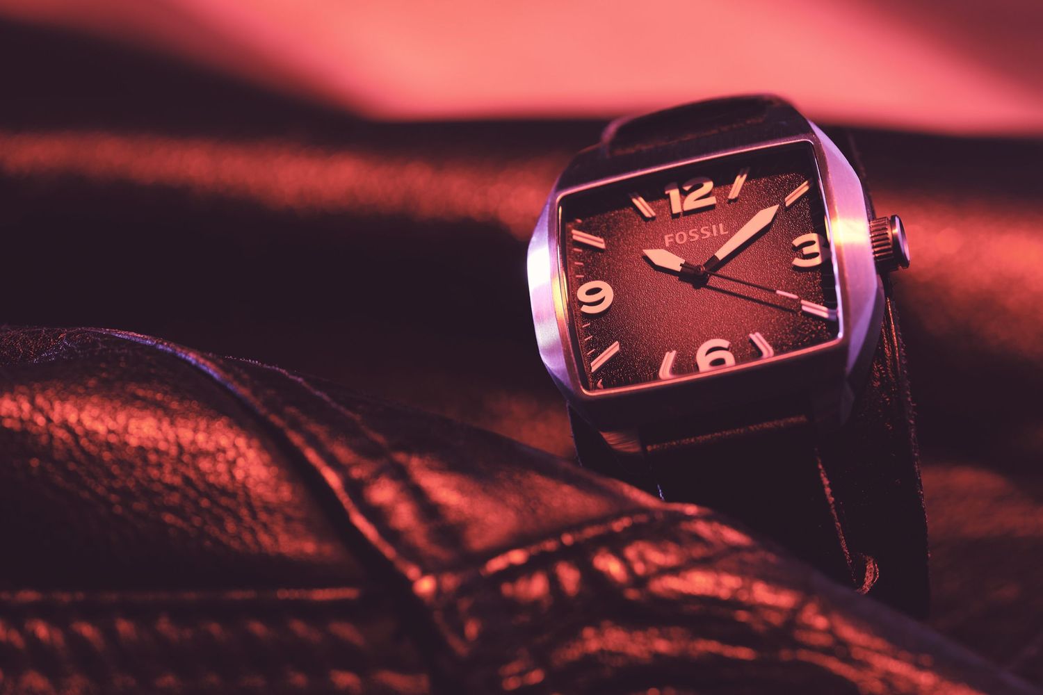 Close-up of a wristwatch face with red ambient lighting creating a moody atmosphere.