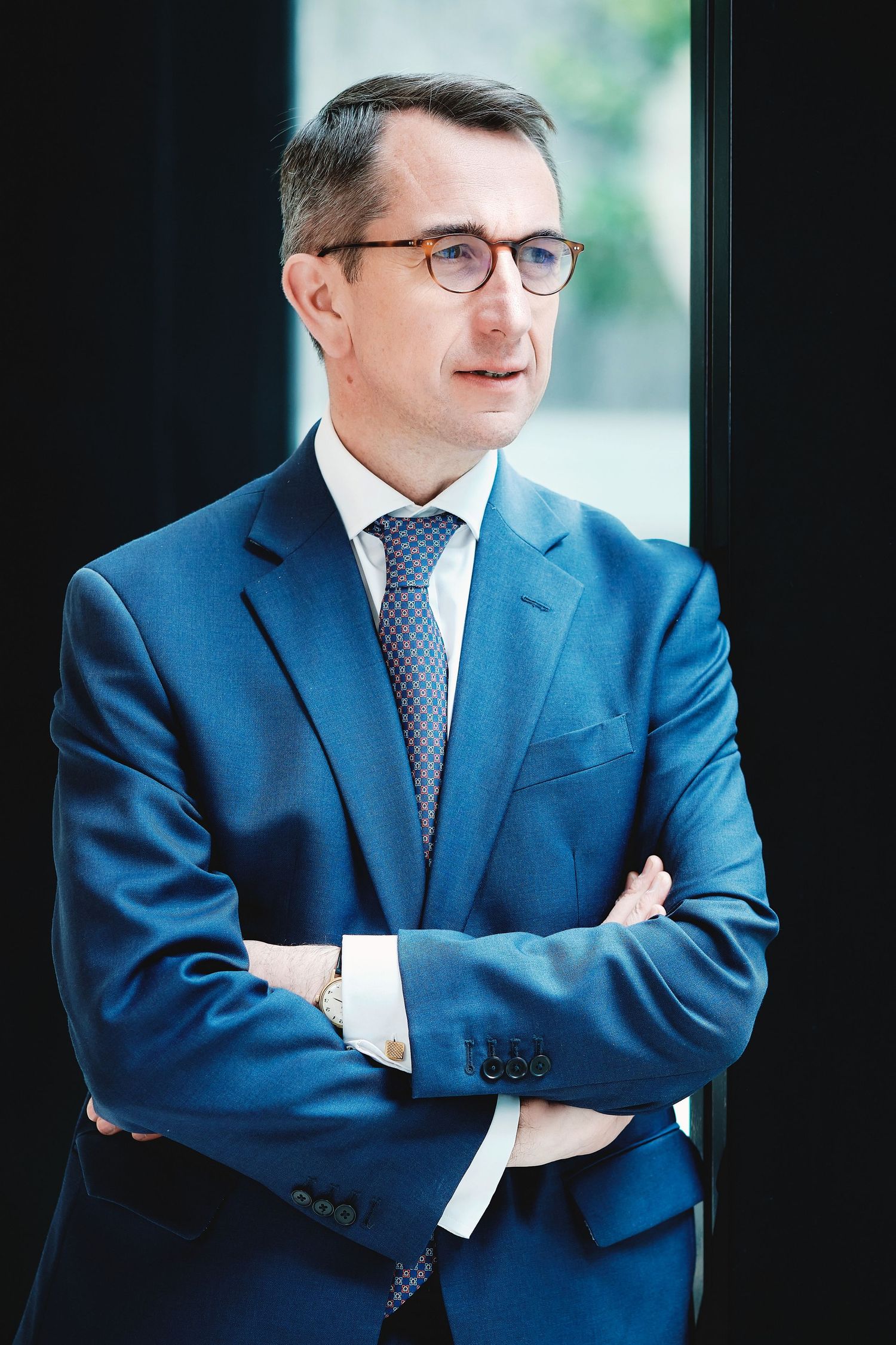 Executive wearing blue suit and glasses in professional corporate headshot.