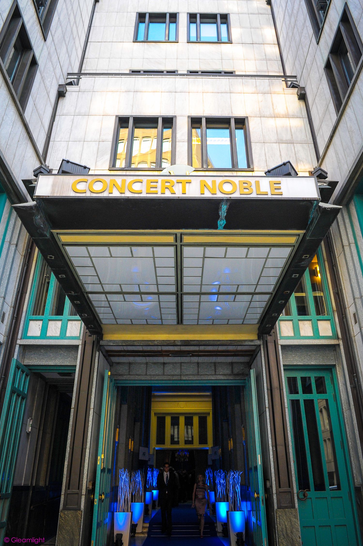 Exterior view of Concert Noble venue entrance with illuminated blue lighting and green doors.