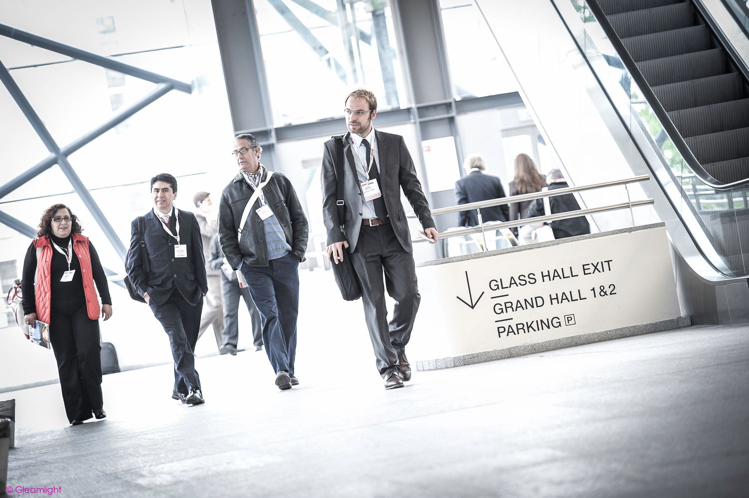 Modern office building interior with escalators and people walking through a bright corridor.