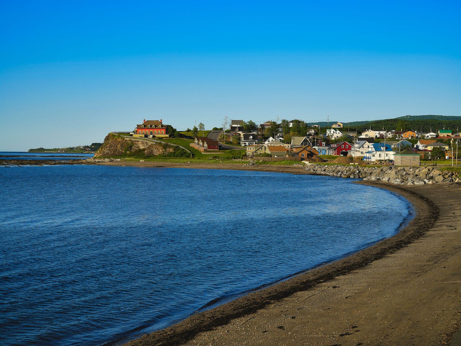 Panoramic view of a coastal town with colorful houses perched on rocky cliffs overlooking a blue ocean bay.