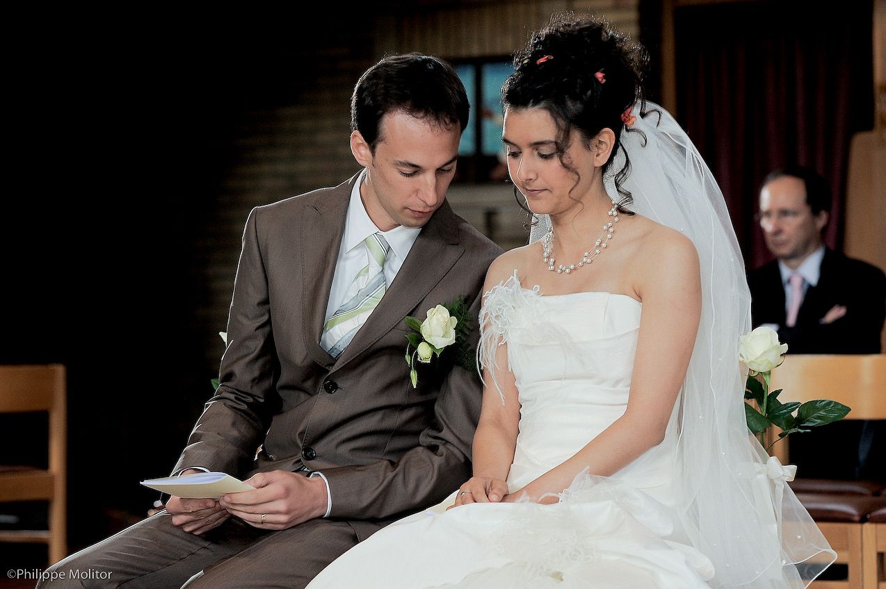 A bride in white gown and groom in gray suit reading vows together during a church wedding ceremony.