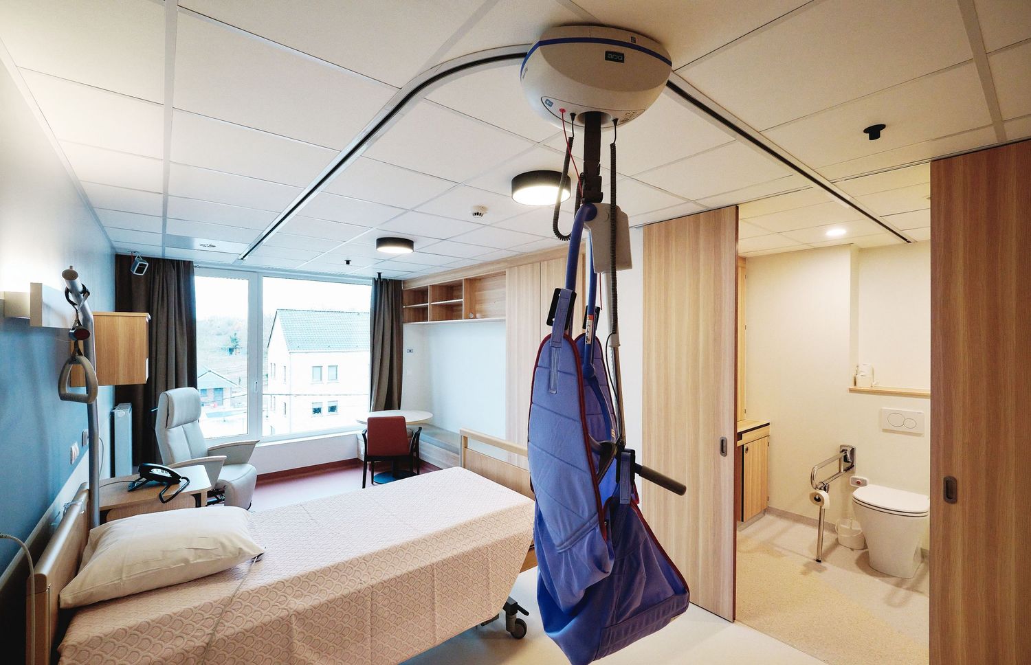 Hospital patient room with medical equipment and adjustable bed in neutral tones.
