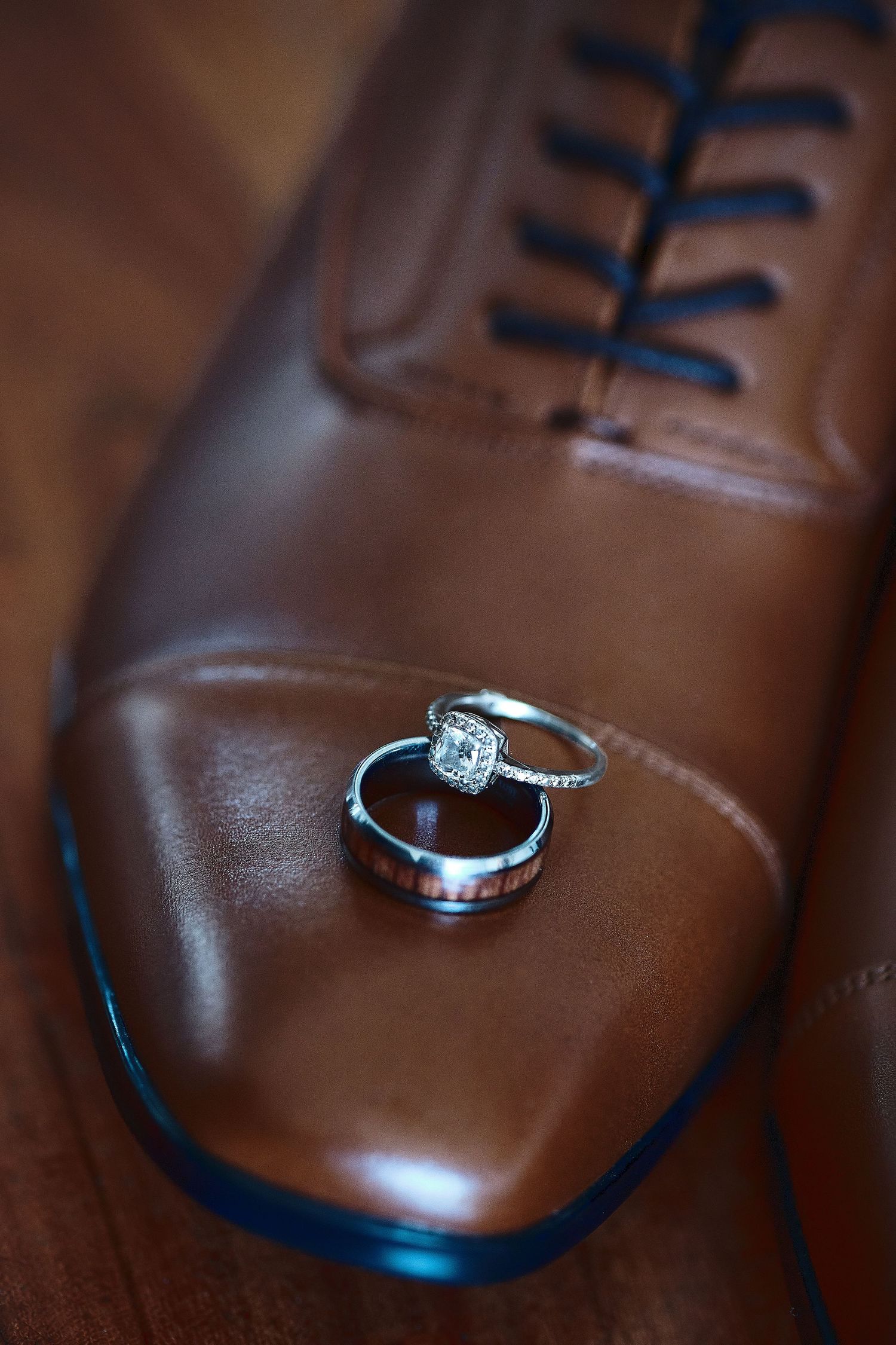 Wedding rings resting on a brown leather dress shoe with dark blue laces for a classic groom detail shot.