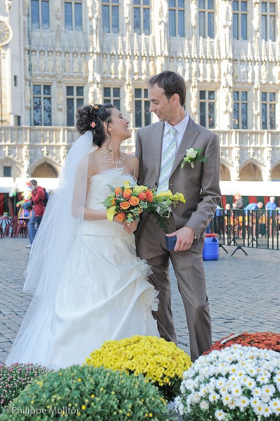 Bride and groom sharing a romantic moment outdoors, holding a colorful bouquet, with a grand historic building in the background.