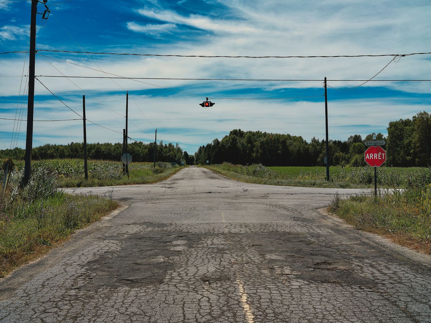 Empty rural road stretches to horizon under blue sky with telephone poles lining the sides.