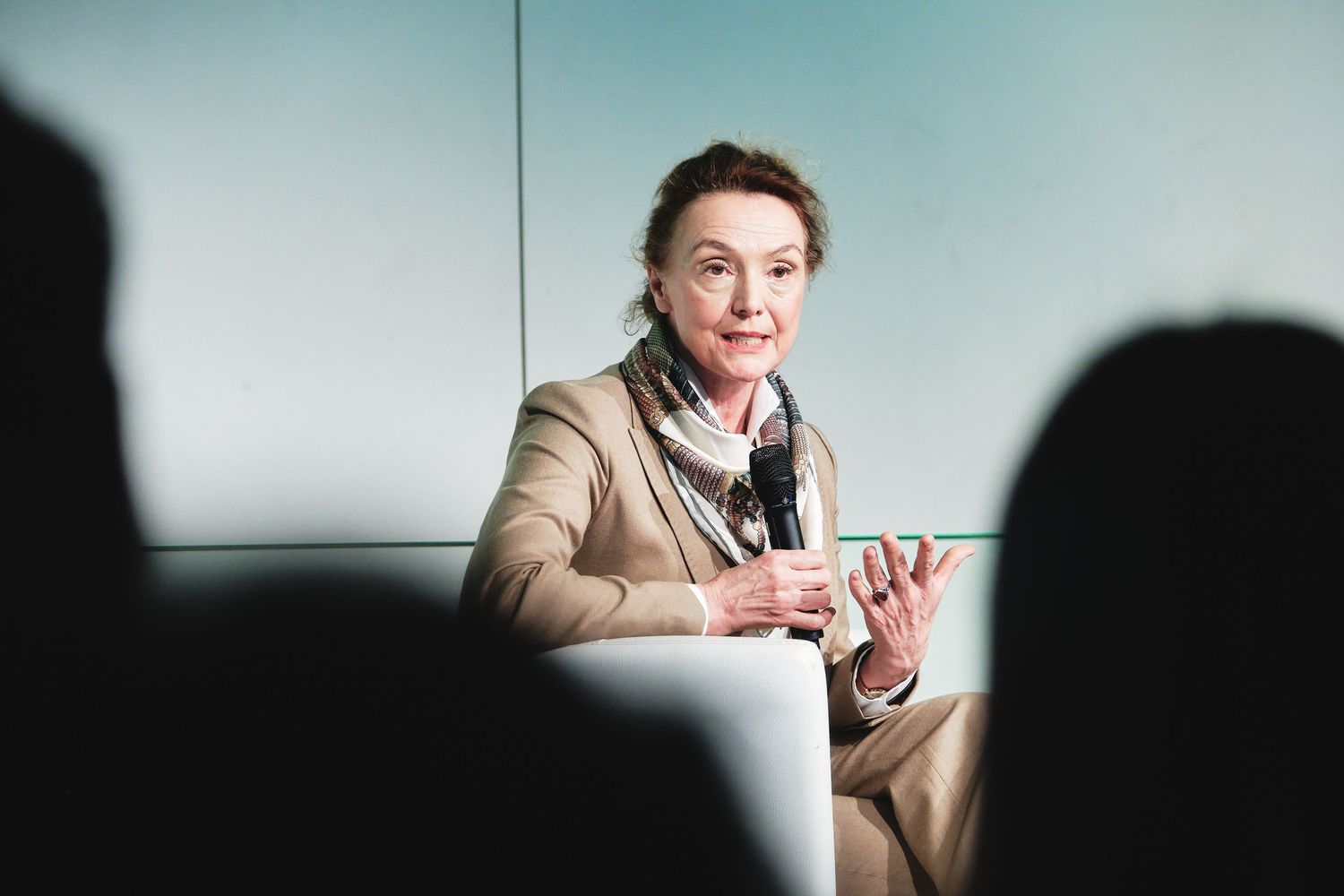 Speaker in beige jacket gestures while participating in conference discussion.
