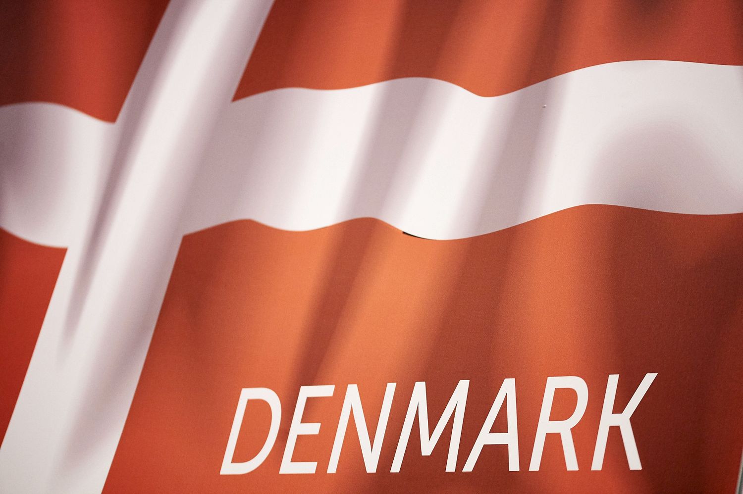 Waving Danish flag with red and white stripes against a bright background.