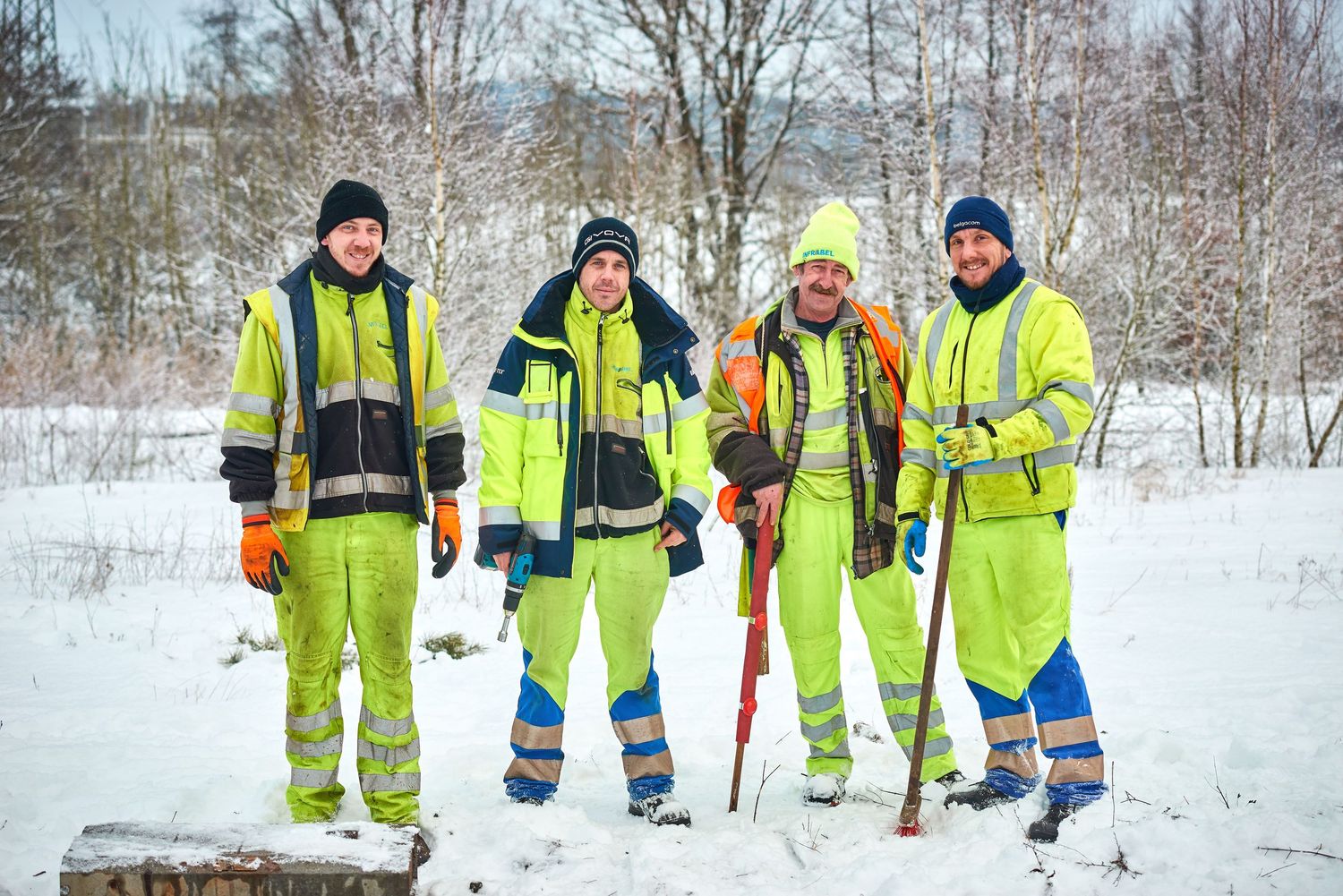Group of railway workers in safety gear stand together on snowy tracks with maintenance tools.